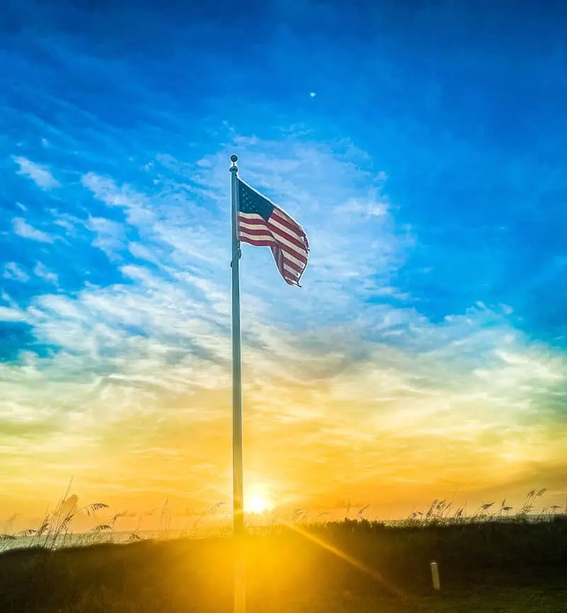 Sunrise on a beach with the American flag waving American flag at sunrise