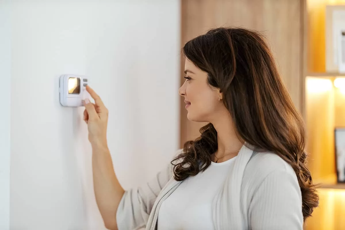 A smiling woman is turning heat on at home.